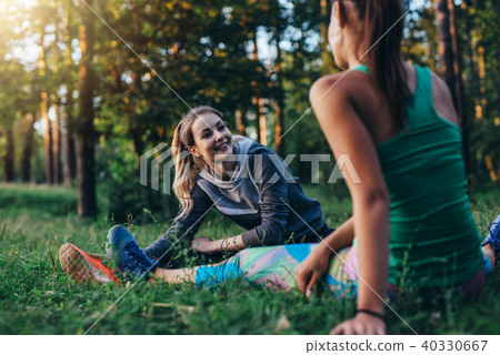 Two cheerful female athletes warming up before training doing stretching exercise for legs sitting Two cheerful female athletes warming up before training doing stretching exercise for legs sitting 40330667