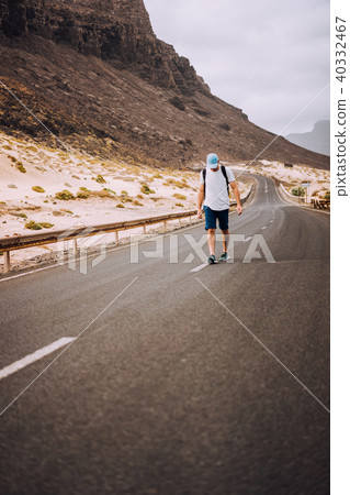 Traveler with backpack standing in the center of an epic winding road. Huge volcanic mountains in Traveler with backpack standing in the center of an epic winding road. Huge volcanic mountains in 40332467