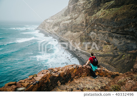 Men hiker with backpack on the scenic coastal road. The route leads along huge volcanic rock cliffs 40332496