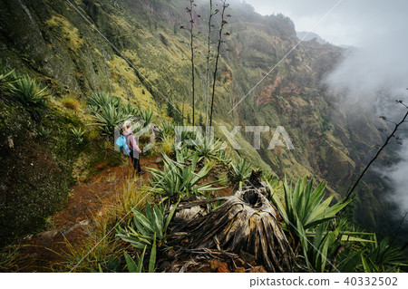 Female traveler staying on the cove volcano edge above the foggy green valley overgrown with agaves Female traveler staying on the cove volcano edge above the foggy green valley overgrown with agaves 40332502