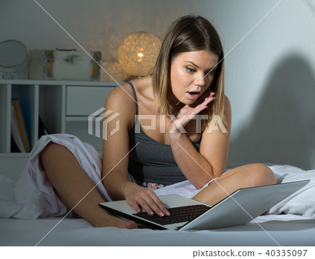 Sexy worried female siting with laptop on bed, holding arm near mouth Sexy worried female siting with laptop on bed, holding arm near mouth 40335097