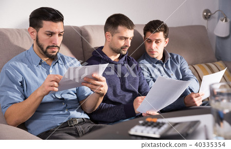 Three serious men discussing documents on sofa Three serious men discussing documents on sofa 40335354