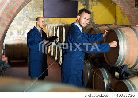 two smiling men in uniforms taking notes in cellar with wine woods 40335720