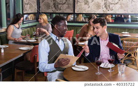 Сheerful male friends choosing dishes from menu card in restaurant 40335722
