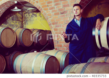 Young friendly man wearing uniform standing in cellar with wine woods 40335733
