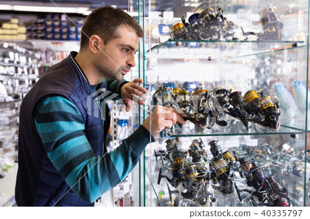 Male choosing baitcasting reel for rod for fishing in the sports shop 40335797