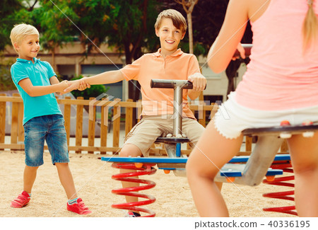 kids are teetering on the swing on the playground. 40336195