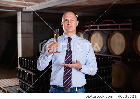 Confident winemaker offering glass of white sparkling wine for tasting in wine cellar 40336521