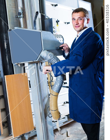 portrait of man in uniform working on large automatic saw machinery indoors 40338316