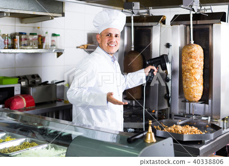 man chef wearing uniform cutting meat for kebab on kitchen in fast food restaurant man chef wearing uniform cutting meat for kebab on kitchen in fast food restaurant 40338806