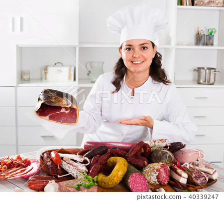 Girl cook costs near table on which sausages and smoked meat Girl cook costs near table on which sausages and smoked meat 40339247