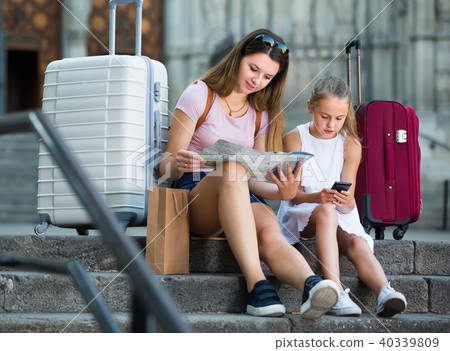 Smiling young woman with daughter travelers looking for destination using city map and phone 40339809