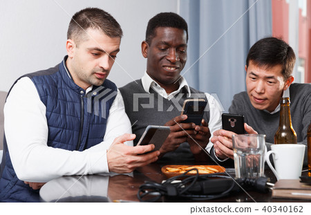 Three friends are chatting each in his phone while relaxing together Three friends are chatting each in his phone while relaxing together 40340162