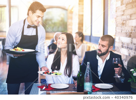 Waiter with dishes serving man and woman friendly company indoors 40340976