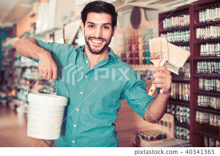 Man standing amongst racks in paint store with brushes and paint 40341365