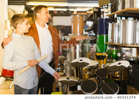 Father and teenage son examining drum units in guitar shop Father and teenage son examining drum units in guitar shop 40341374