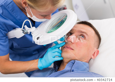 Woman specialist is cleaning skin of patient with using magnification before the procedure 40342714