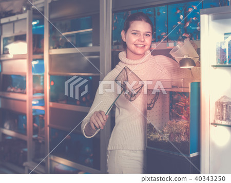 Girl holding aquarian net and water container next to aquarium with colorful fish in aquarium shop Girl holding aquarian net and water container next to aquarium with colorful fish in aquarium shop 40343250