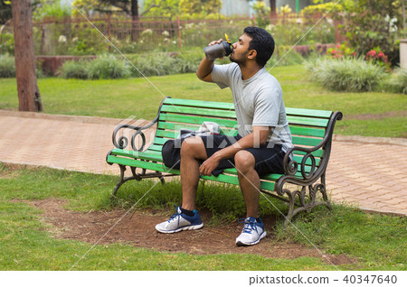 Young athlete drinking water while resting in park 40347640