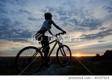 Side view of young lady cycling in mountains with an evening landscape Side view of young lady cycling in mountains with an evening landscape 40347924