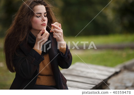 Young beautiful woman applying lipstick outdoors 40359478