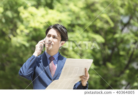 Talking on a smartphone while holding a businessman and an English newspaper 40364805