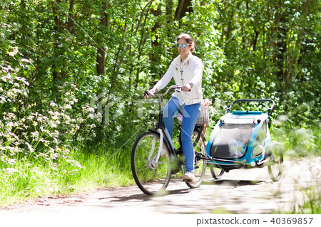 Mother on bicycle with baby bike trailer in park Mother on bicycle with baby bike trailer in park 40369857