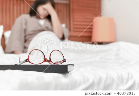 eyeglasses on book and blurred woman on bed  40378013