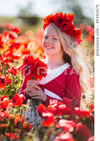 Cute smiling blonde child girl is wearing wreath from red flowers in poppy field 40391678