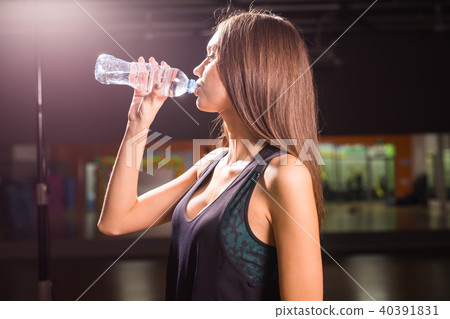 Fitness young woman drinking water in the gym. Muscular woman taking break after exercise Fitness young woman drinking water in the gym. Muscular woman taking break after exercise 40391831