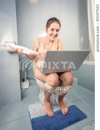 Toned photo of young smiling woman sitting on toilet with computer Toned photo of young smiling woman sitting on toilet with computer 40397502