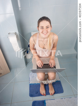 Portrait of young smiling woman sitting on toilet and working on laptop Portrait of young smiling woman sitting on toilet and working on laptop 40397504