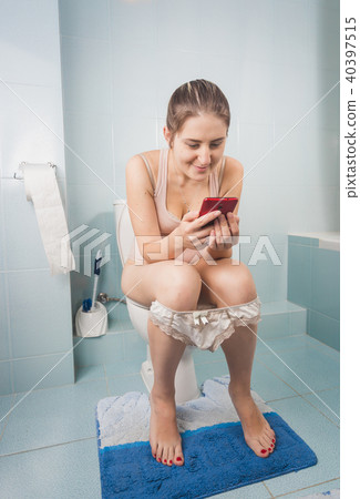 Young brunette woman addicted to mobile phone sitting on toilet and using smartphone 40397515