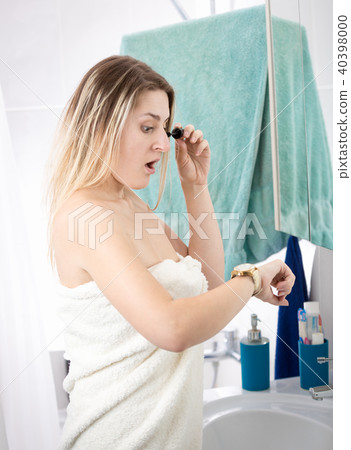 Portrait of young woman doing makeup in bathroom and looking at wristwatch 40398000