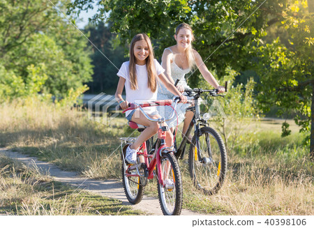 Happy smiling girl riding bicycle with young mother in field at hot summer day 40398106