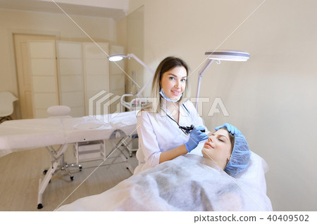 Woman at cosmetology cabinet getting tattooing eyebrows by cosmetologist. 40409502