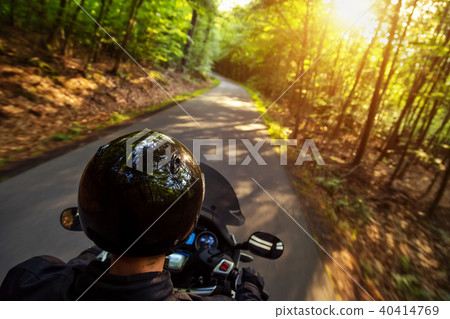Close-up of motorbiker riding on empty road in forest Close-up of motorbiker riding on empty road in forest 40414769