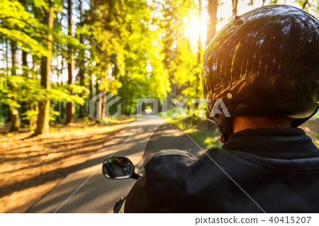 Close-up of motorbiker riding on empty road in forest 40415207