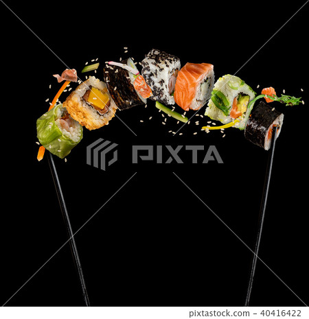 Sushi pieces placed between chopsticks on black background 40416422
