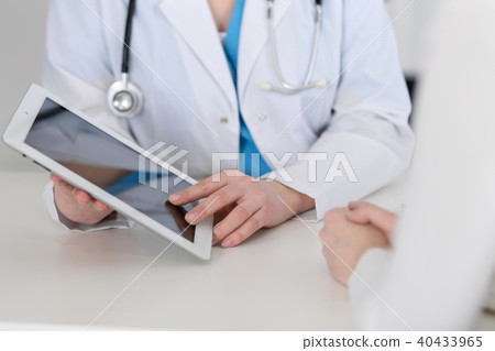 Closeup of a doctor and  patient  sitting at the desk. Physician pointing into tablet pc. Medici 40433965