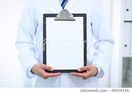 Unknown male doctor standing straight while holding medical clipboard with blank white paper 40434140