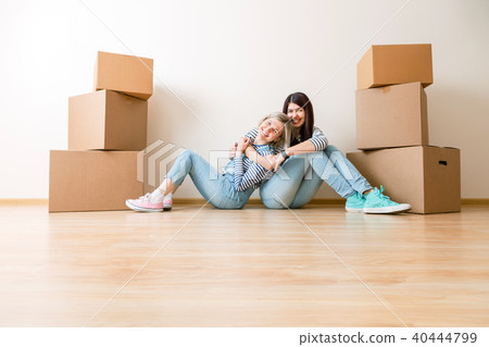 Photo of two girls sitting on floor among cardboard boxes 40444799