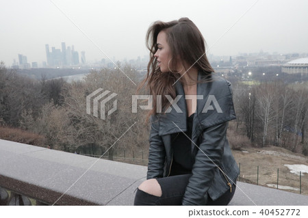 Stylish young woman sitting on the bridge overlooking the city. Stylish young woman sitting on the bridge overlooking the city. 40452772