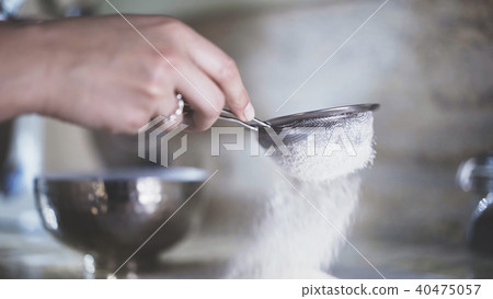 A woman sifting a flour through a sieve A woman sifting a flour through a sieve 40475057