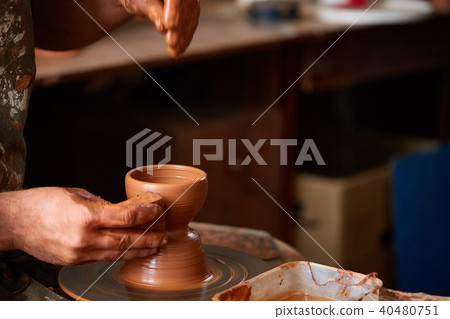Close-up hands of a male potter in apron making a vase from clay, selective focus Close-up hands of a male potter in apron making a vase from clay, selective focus 40480751