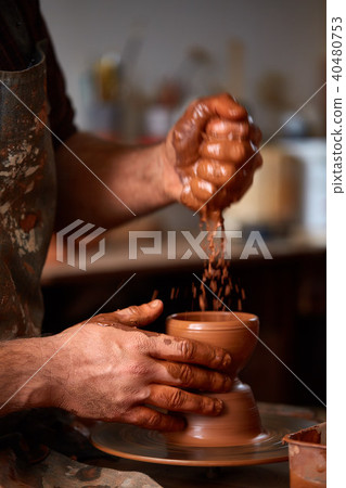 Close-up hands of a male potter in apron making a vase from clay, selective focus Close-up hands of a male potter in apron making a vase from clay, selective focus 40480753