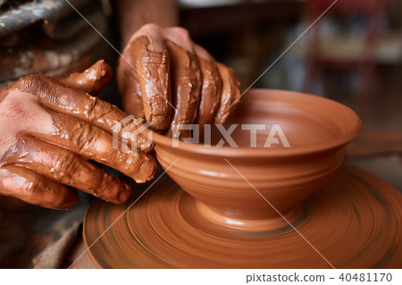Close-up hands of a male potter in apron making a vase from clay, selective focus Close-up hands of a male potter in apron making a vase from clay, selective focus 40481170