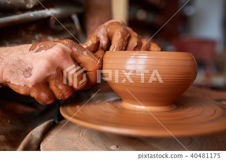 Close-up hands of a male potter in apron making a vase from clay, selective focus Close-up hands of a male potter in apron making a vase from clay, selective focus 40481175