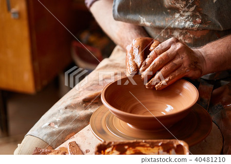 Close-up hands of a male potter in apron making a vase from clay, selective focus Close-up hands of a male potter in apron making a vase from clay, selective focus 40481210