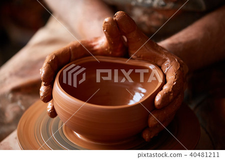 Close-up hands of a male potter in apron making a vase from clay, selective focus Close-up hands of a male potter in apron making a vase from clay, selective focus 40481211